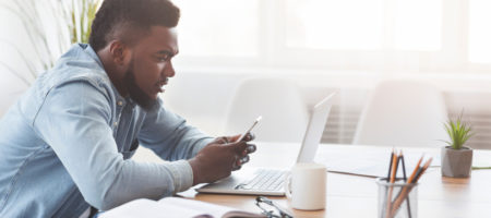 A person working remotely with a phone in their hand and a laptop open in front of them.