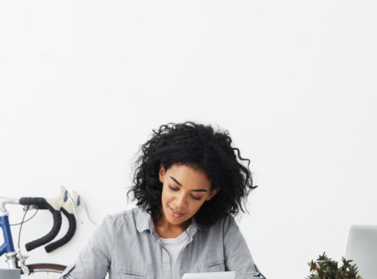 A person sitting at their desk, writing on paper and holding an iPad in their hand.