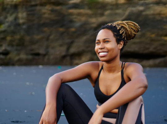 A person wearing work-out attire, sitting on the ground with a big smile on their face.