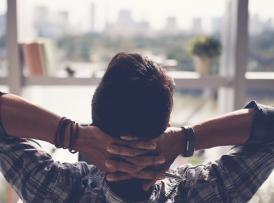 Person sits with arms behind head staring out a window