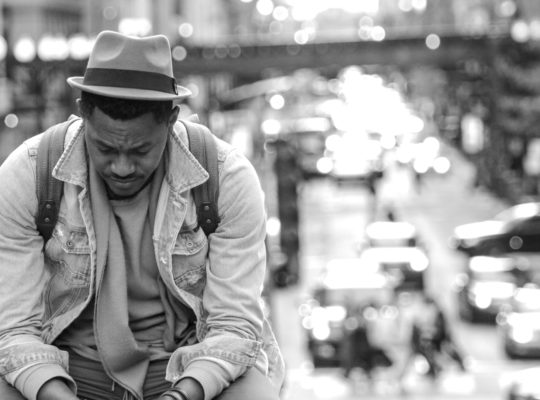 person is seated next to a city street and is looking at their hands with a look of concern on their face.