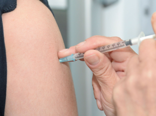 A person having a flu vaccine injected in their upper arm