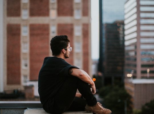 A person sits on the ledge of a building staring out at the city