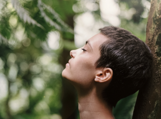 Person leaning back against a tree with closed eyes.