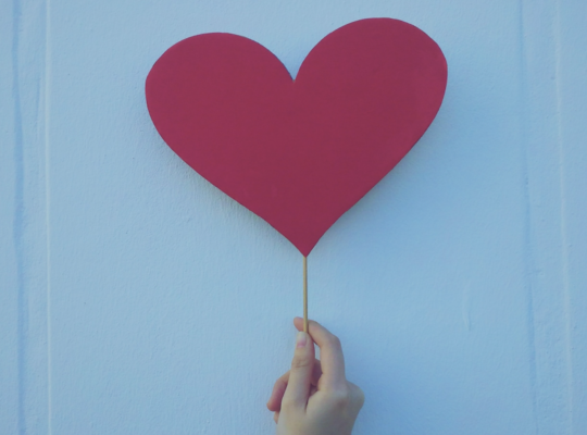 a hand holding a red paper heart
