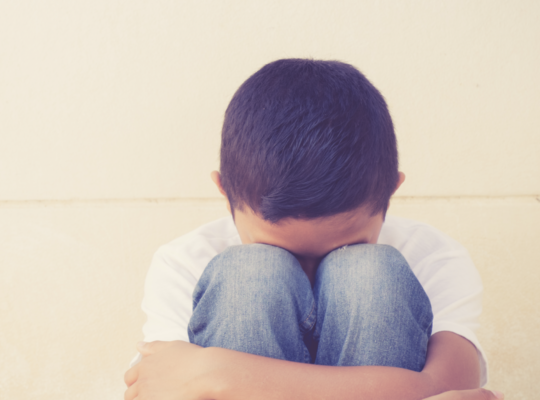 A child seated on the ground with his head down hugging his knees