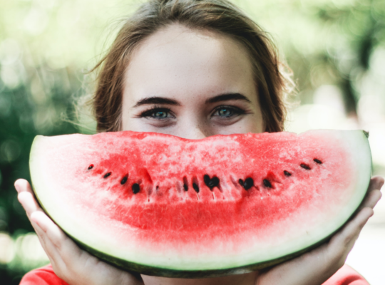 Person holding up a big slice of watermelon to their face.