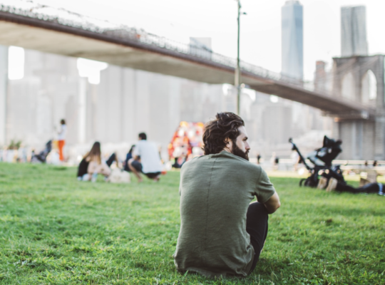 man sitting on the grass in a park staring off into the distance
