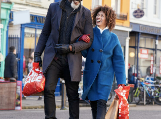 a married couple linking arms and holding shopping bags as they walk down a street