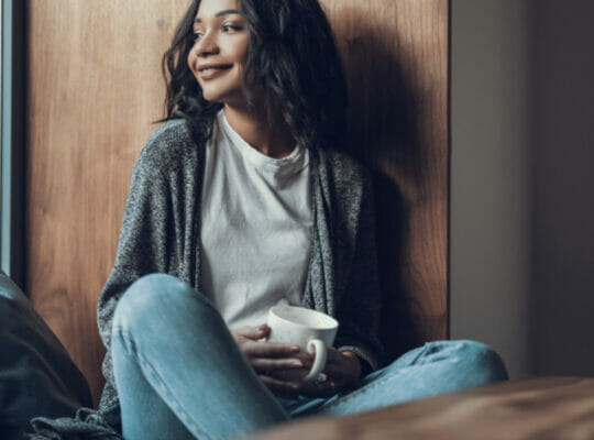 person staring off into the distance with a big smile on their face and a cup of coffee in their hand.