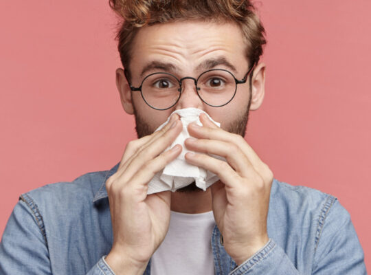 person blowing their nose into a tissue.