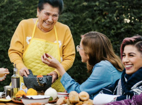 A group of people are all smiling and in deep conversation at a table filled with food.