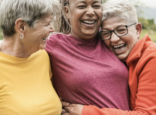 three people are hugging with smiles on their faces.